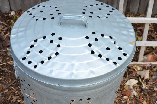 A metal trash can with holes punched in the lid and on the sides, used as a compost bin.