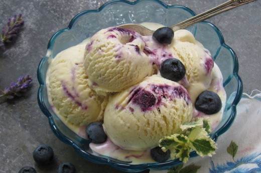 A dish of blueberry lavender ice cream, with blueberries sprinkled on top and lavender next to the dish.