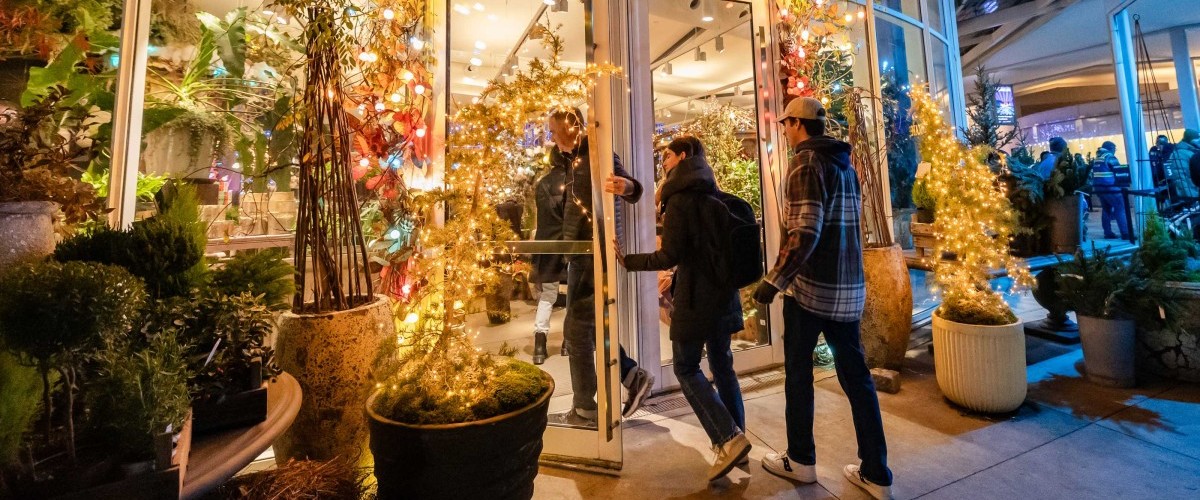 At night, people enter a store filled with plants and sparkling lights.